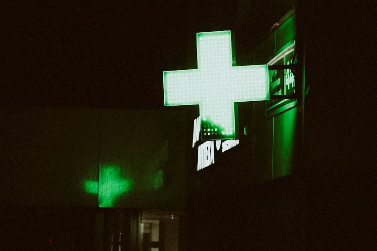 Glowing pharmacy cross sign at night for emergency pharmacy access in Queens